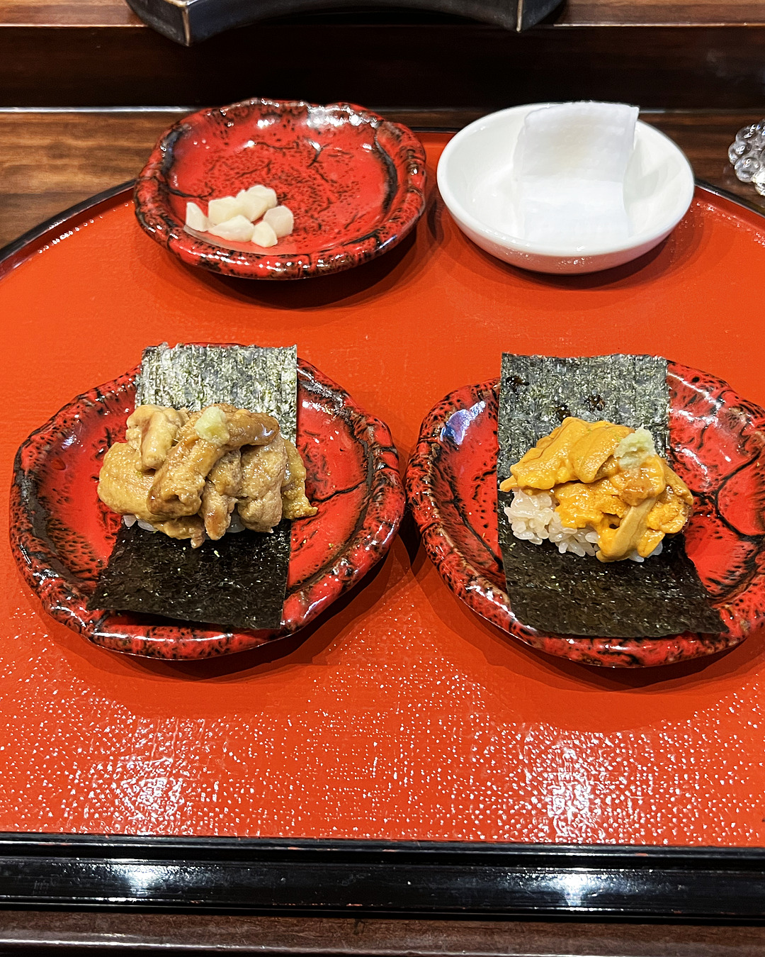 Two uni nigiri side by side on red lacquer plates, pale murasaki on the left, vivid orange bafun on the right.